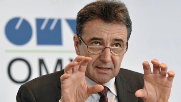 Ein Mann mit Brille gestikuliert vor einem Logo.