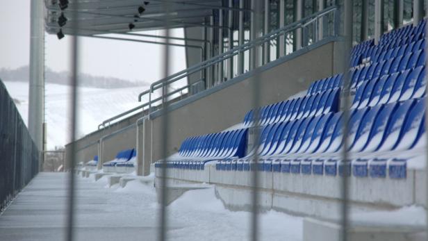 Schnee bedeckt die blauen Sitze in einem leeren Stadion.
