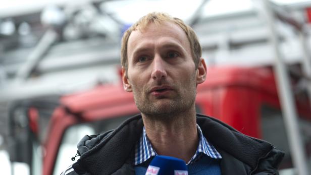 Ein Mann mit Mikrofon steht vor einem roten Feuerwehrauto.