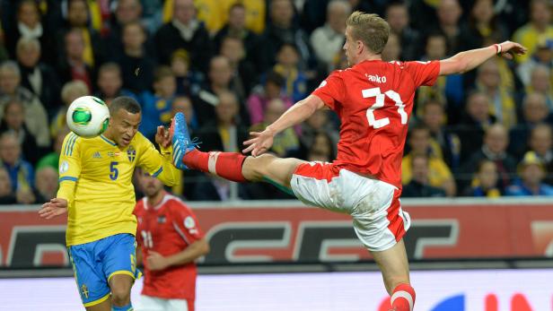 Ein Fußballspieler in Rot tritt gegen einen schwedischen Spieler um den Ball.
