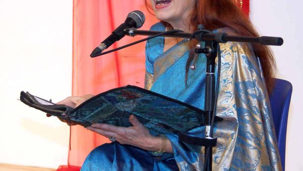 Eine Frau in einem blauen Sari liest von einem Mikrofon aus einem Buch vor.