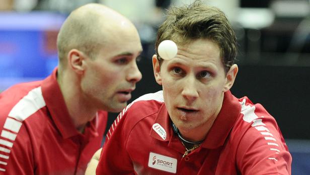 Zwei Tischtennisspieler während eines Spiels, der Ball berührt die Stirn eines Spielers.
