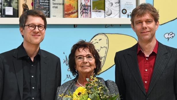 Drei Personen posieren vor einem Bücherregal und einer Wandmalerei.