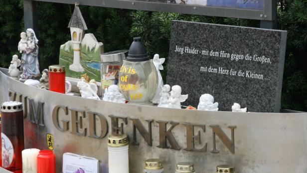 Eine Gedenkstätte für Jörg Haider mit Engeln, Kerzen und einem beschrifteten Stein.
