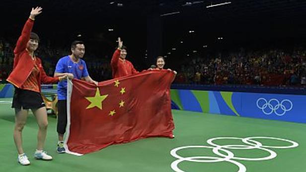 Chinesische Tischtennisspieler feiern mit der chinesischen Flagge bei den Olympischen Spielen.