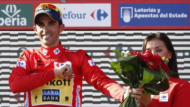 Ein Radrennfahrer in roter Kleidung mit einem Blumenstrauß auf einem Podium.
