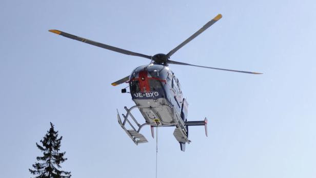 Ein Hubschrauber mit der Aufschrift „UE-BXG“ fliegt vor blauem Himmel.