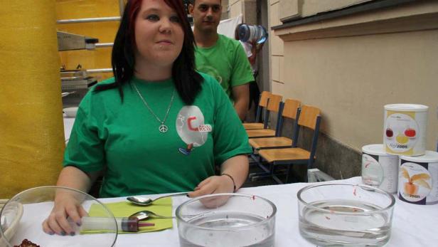 Eine Frau mit einem grünen T-Shirt steht an einem Tisch mit Schüsseln und Spritzen.