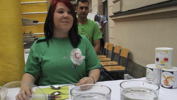 Eine junge Frau mit einem grünen T-Shirt steht an einem Tisch mit Reagenzien und Behältern.