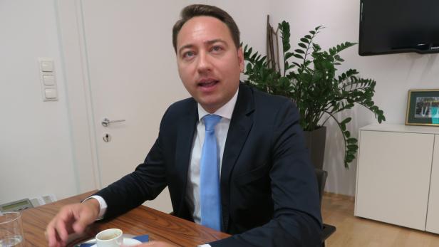 Ein Mann im Anzug sitzt an einem Tisch mit einer Tasse Kaffee.