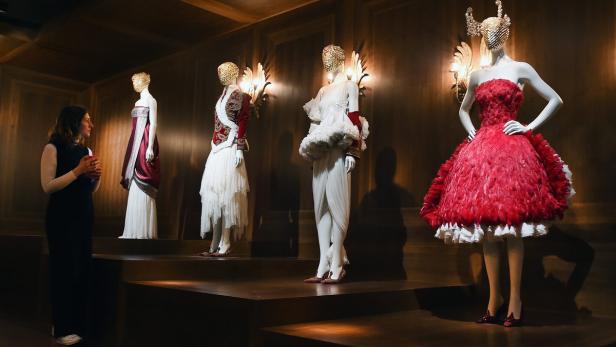 Eine Frau betrachtet in einem Museum eine Ausstellung von Kleidern auf Schaufensterpuppen.