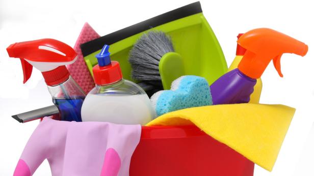Ein roter Eimer gefüllt mit verschiedenen Reinigungsutensilien wie Sprays, Schwämmen und Tüchern.