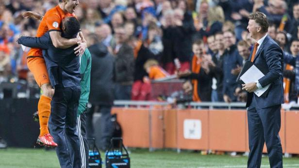 Ein Fußballspieler wird von einem Teamkollegen umarmt, während der Trainer lächelt.