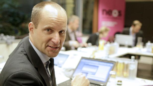 Ein Mann im Anzug sitzt an einem Tisch mit Laptops und anderen Personen.