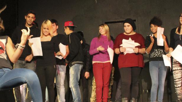 Eine Gruppe junger Leute steht auf einer Bühne und hält Papier in den Händen.