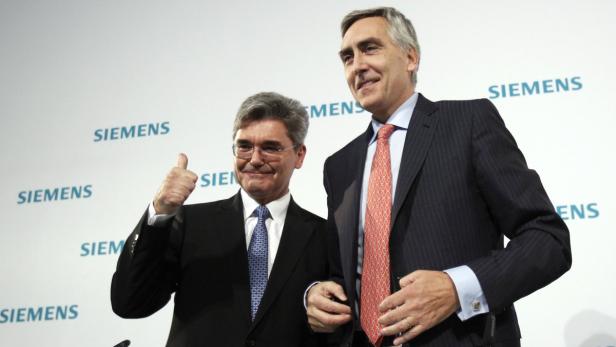 Zwei Männer in Anzügen posieren vor einem Siemens-Logo.