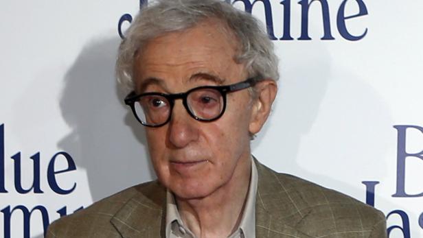 Woody Allen mit Brille posiert vor einer Werbewand.
