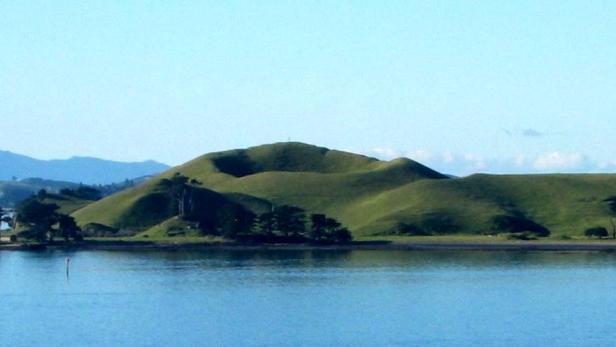 Hügelige grüne Landschaft am Wasser unter blauem Himmel.