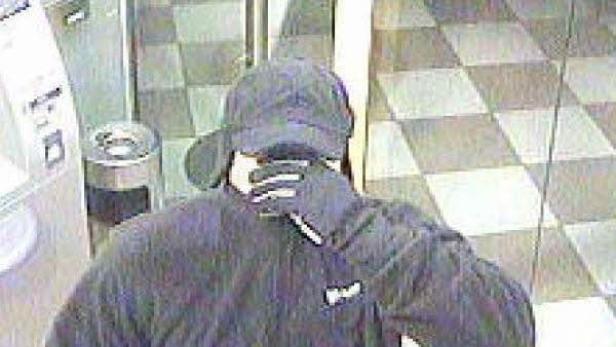 Eine Person mit Mütze und Handschuhen steht vor einem Geldautomaten.