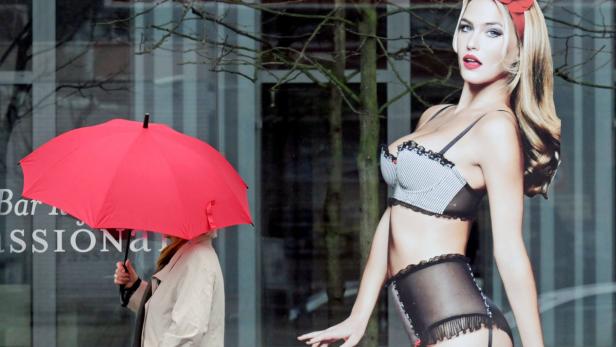 Bei leichtem Sprühregen und Temperaturen um die 9 Grad geht eine Frau mit einem roten Regenschirm am 06.01.2013 in Düsseldorf (Nordrhein-Westfalen) an einem Plakat mit einer Frau in Dessous vorbei, das ans Fenster eines Bürogebäudes geklebt ist. Foto: Horst Ossinger/dpa +++(c) dpa - Bildfunk+++