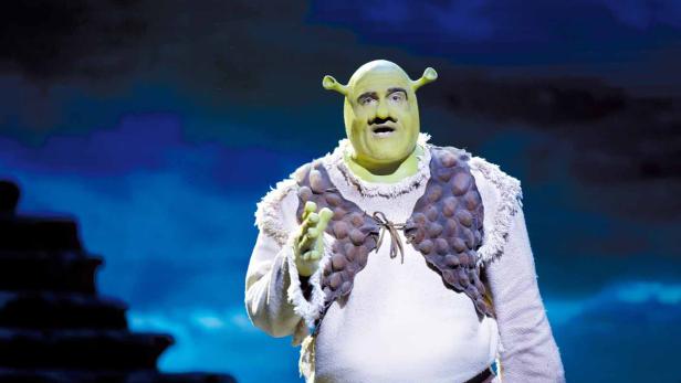 Ein Schauspieler in einem Shrek-Kostüm auf einer Bühne.