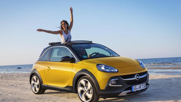Ein gelber Opel Adam Rocks fährt am Strand entlang, eine Frau steht mit erhobenen Armen im offenen Dach.