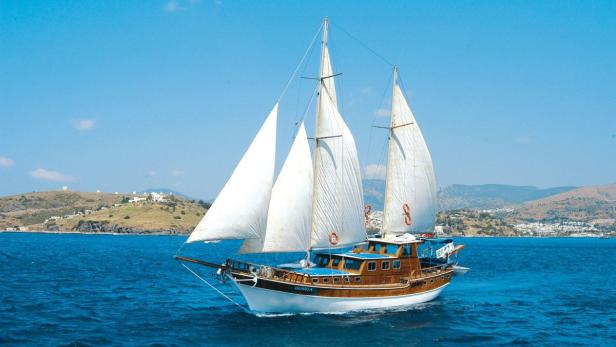 Ein Segelboot fährt auf dem blauen Meer entlang der Küste.