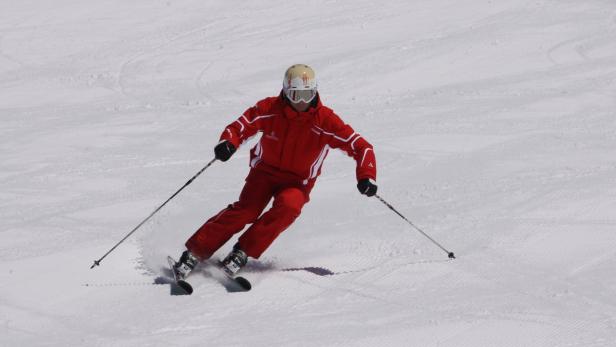 Ein Skifahrer in roter Kleidung fährt eine schneebedeckte Piste hinunter.