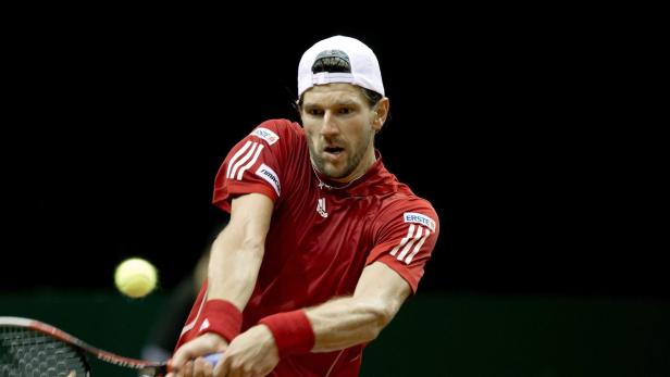 Ein Tennisspieler in rotem Hemd schlägt einen Ball.