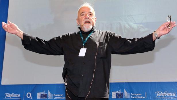 Ein Mann mit Mikrofon gestikuliert mit einer Brille in der Hand vor Logos der EU und Telefónica.
