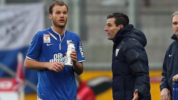 Ein Fußballspieler mit Wasserflasche spricht mit seinem Trainer.