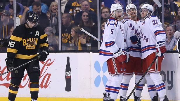 Ein enttäuschter Spieler der Boston Bruins steht vor jubelnden Spielern der New York Rangers.