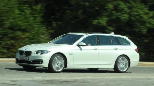 Ein weißer BMW 5er Touring fährt auf einer Straße.