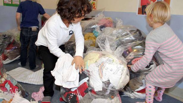 Drei Kinder wühlen in Säcken voller Kleidung.