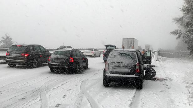 Schneechaos auf der Autobahn mit stehenden Autos und einem Mann am Straßenrand.