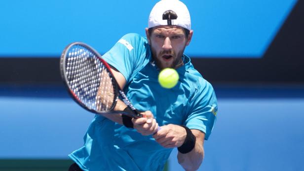 Ein Tennisspieler schlägt einen gelben Tennisball vor einem blauen Hintergrund.