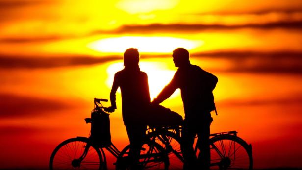 Ein Paar steht mit Fahrrädern im Gegenlicht eines Sonnenuntergangs.