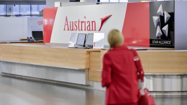 Ein Check-in-Schalter von Austrian Airlines mit einer Frau im roten Blazer im Vordergrund.