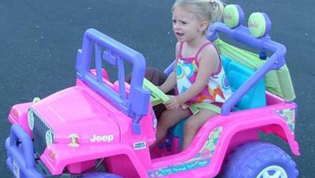 Ein kleines Mädchen fährt in einem pinkfarbenen Jeep-Spielzeugauto.