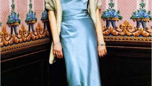 Eine Frau in einem hellblauen Kleid und einer Stola posiert vor einer floralen Tapete.