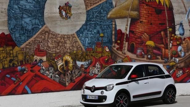 Ein weißer Renault Twingo parkt vor einer Wand mit einem bunten Graffiti.