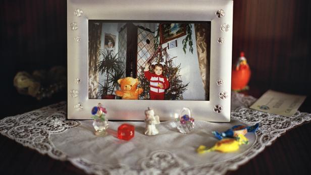 Ein Foto in einem Rahmen zeigt ein kleines Mädchen mit einem Teddybären vor einem Weihnachtsbaum.