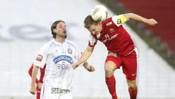 Ein Fußballspieler köpft den Ball, während ein anderer Spieler zusieht.