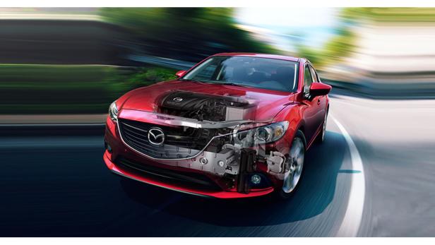 Ein roter Mazda fährt auf einer kurvigen Straße, wobei die Mechanik teilweise sichtbar ist.