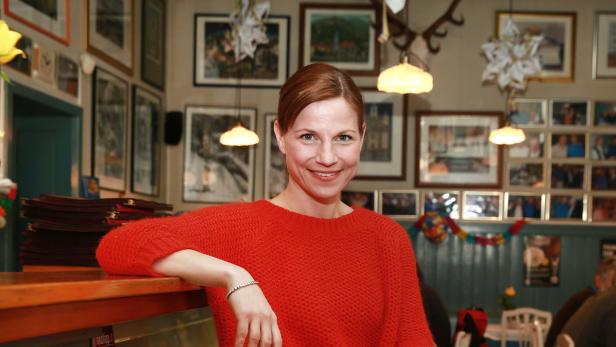 Eine lächelnde Frau in einem roten Pullover lehnt an einer Theke in einem Restaurant.