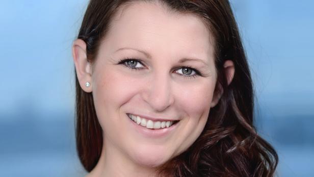 Eine lächelnde Frau mit braunen Haaren und einem Ohrring vor einem blauen Hintergrund.