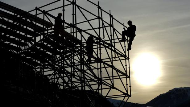 Silhouette von Bauarbeitern auf einem Gerüst vor dem Hintergrund der untergehenden Sonne.
