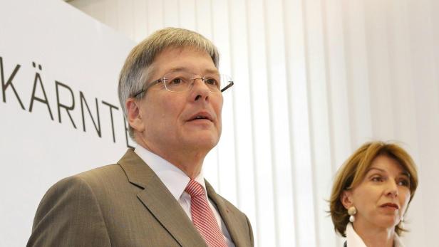 Ein Mann im Anzug und eine Frau stehen nebeneinander vor einem weißen Hintergrund.