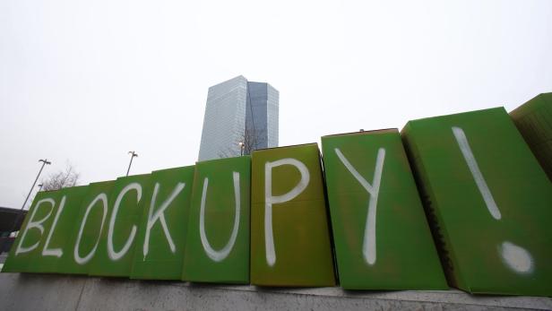 Grüne Kisten mit der Aufschrift „BLOCK UPY!“ stehen vor einem Hochhaus.