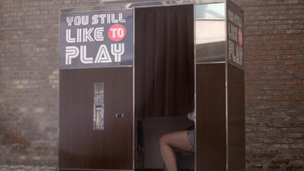 Ein Fotoautomat mit der Aufschrift „You still like to play“ vor einer Backsteinmauer.